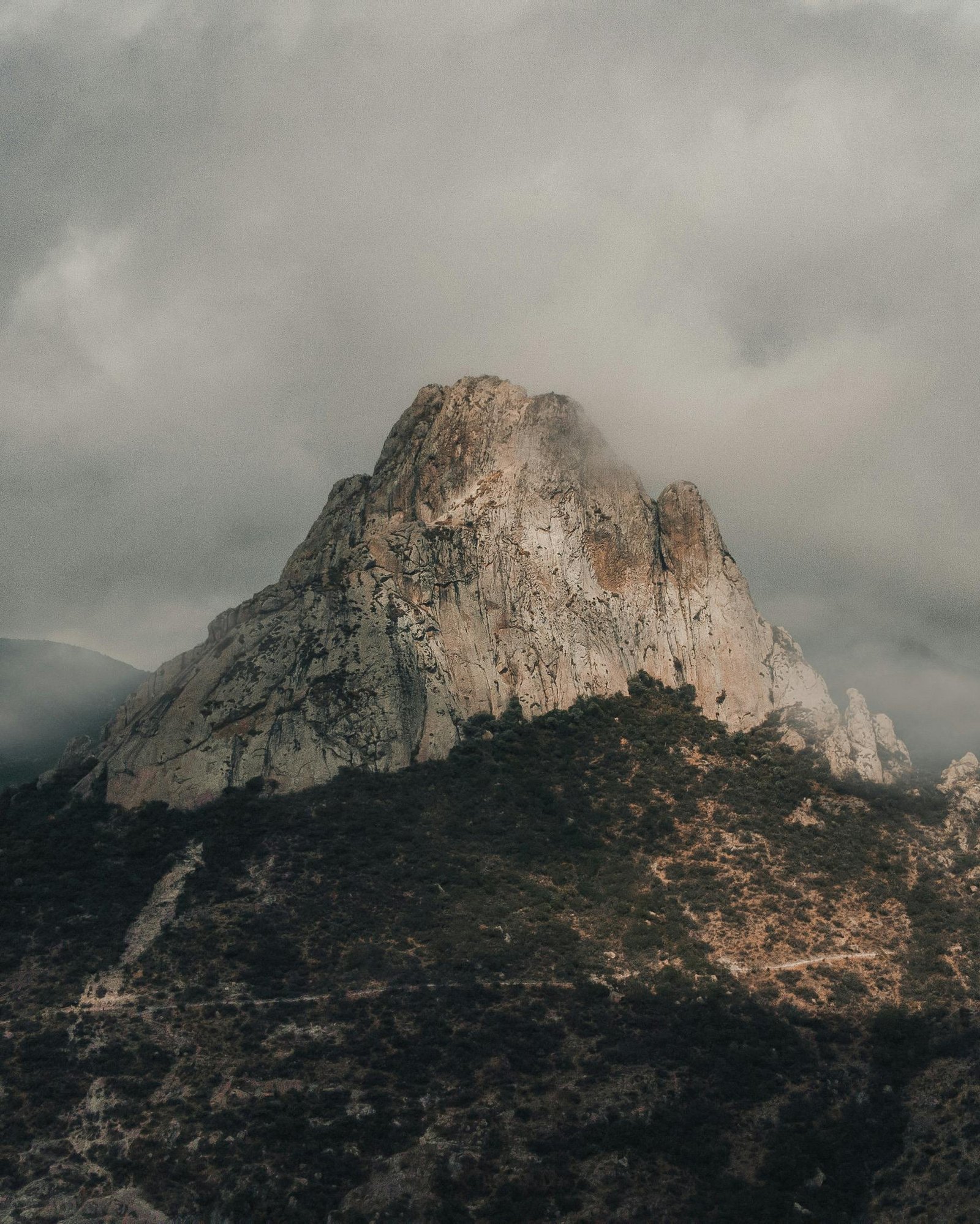 imponente formación rocosa, montaña escarpada, que se eleva de manera majestuosa entre nubes densas y cielo nublado.